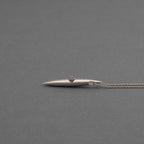 Sterling silver necklace with an elongated crystal-lined spike pendant, resting on a softly spotlighted neutral surface.