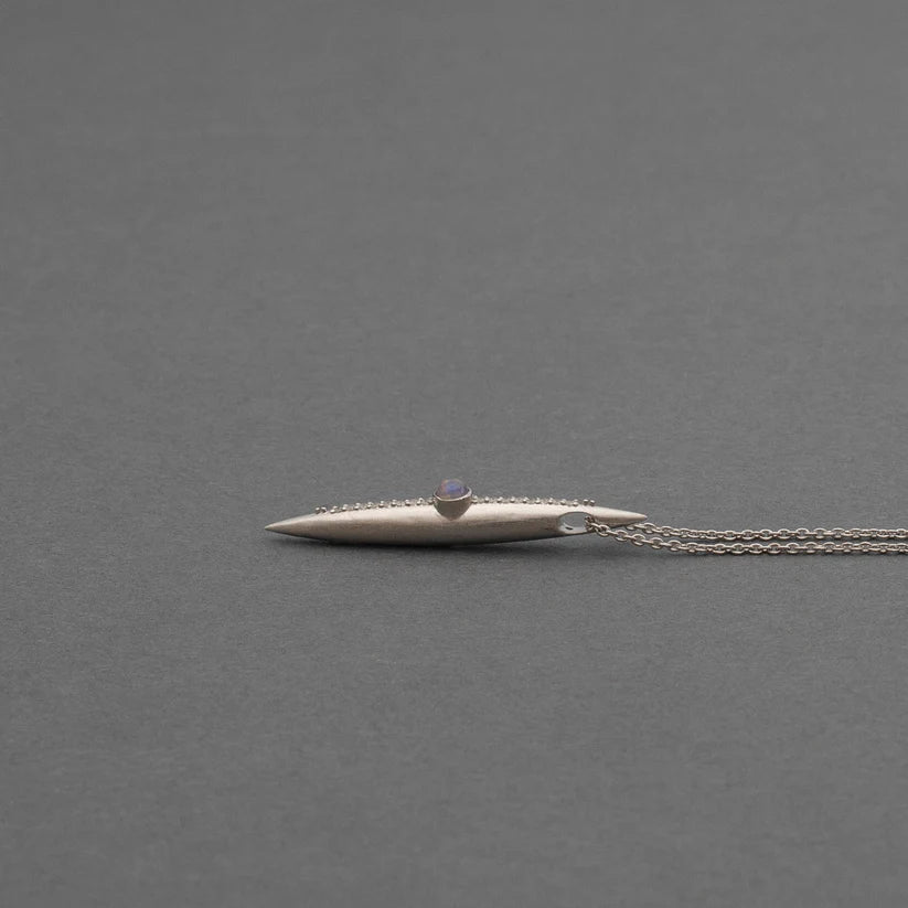 Sterling silver necklace with an elongated crystal-lined spike pendant, resting on a softly spotlighted neutral surface.