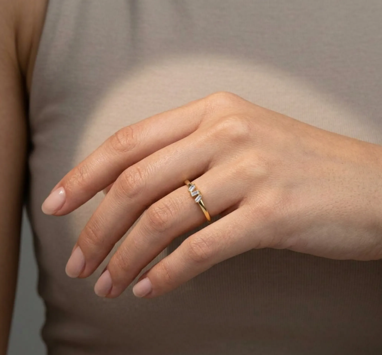 Delicate gold ring with a two-stone crystal accent, standing upright on a softly spotlighted neutral surface.