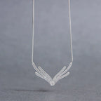 Celebrity-style sterling silver necklace with a crystal-lined wing pendant, hanging on a fine chain against a grey backdrop.